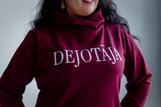 Person wearing a burgundy sweater with 'DEJOTĀJA' text on a plain background