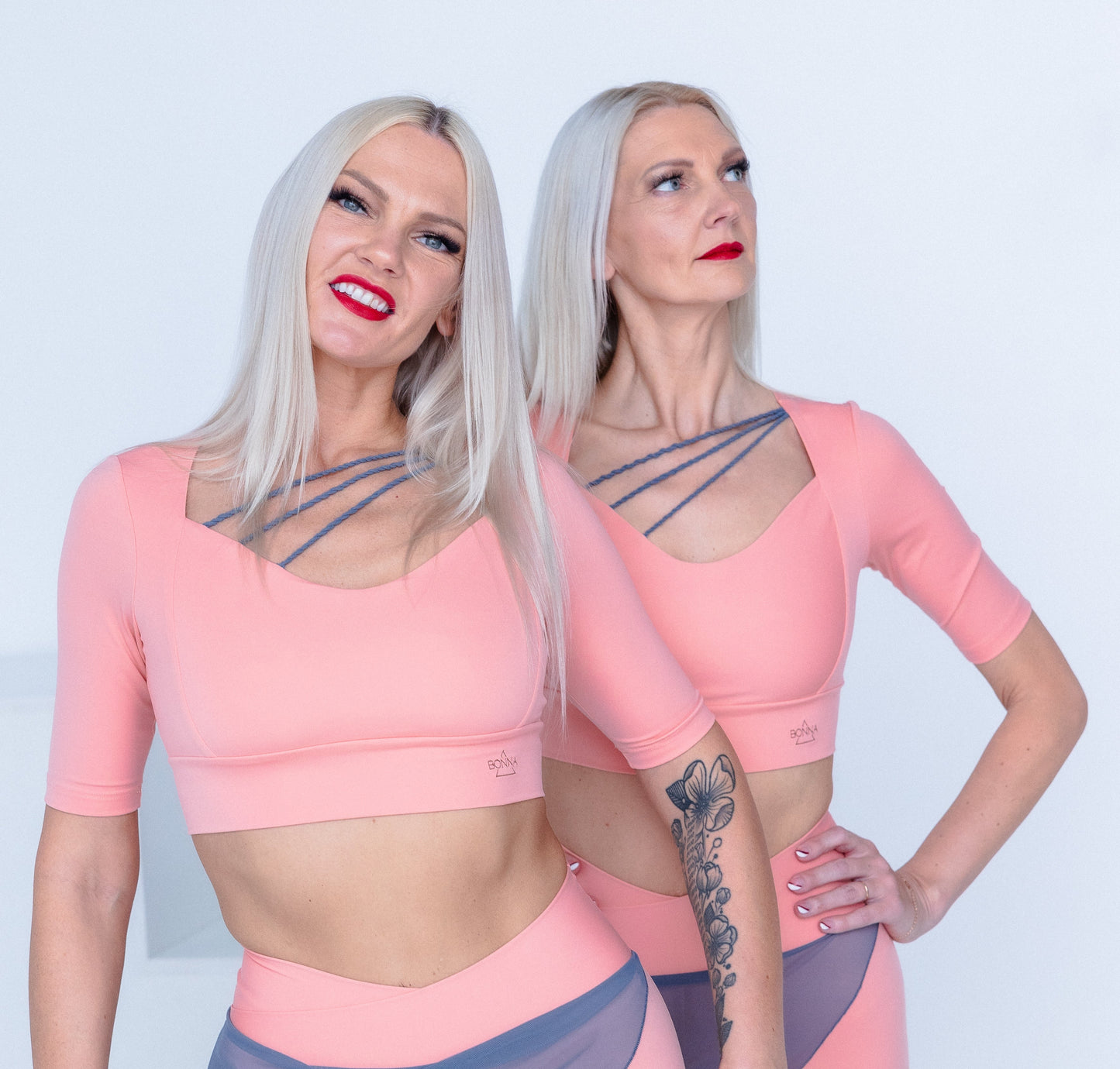 Two women wearing matching pink and gray athletic outfits on a white background
