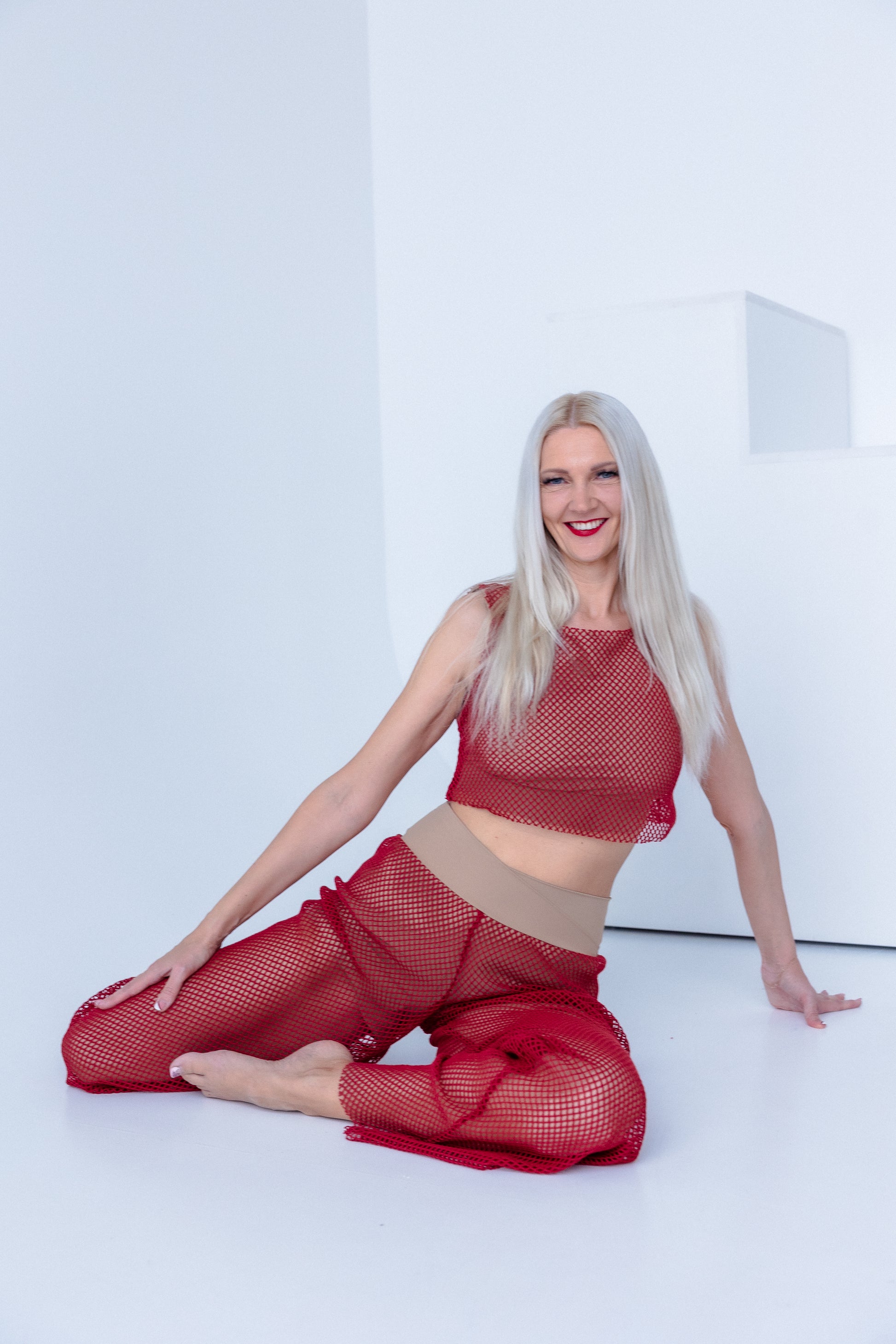 Woman wearing a red mesh outfit sitting on a white floor.