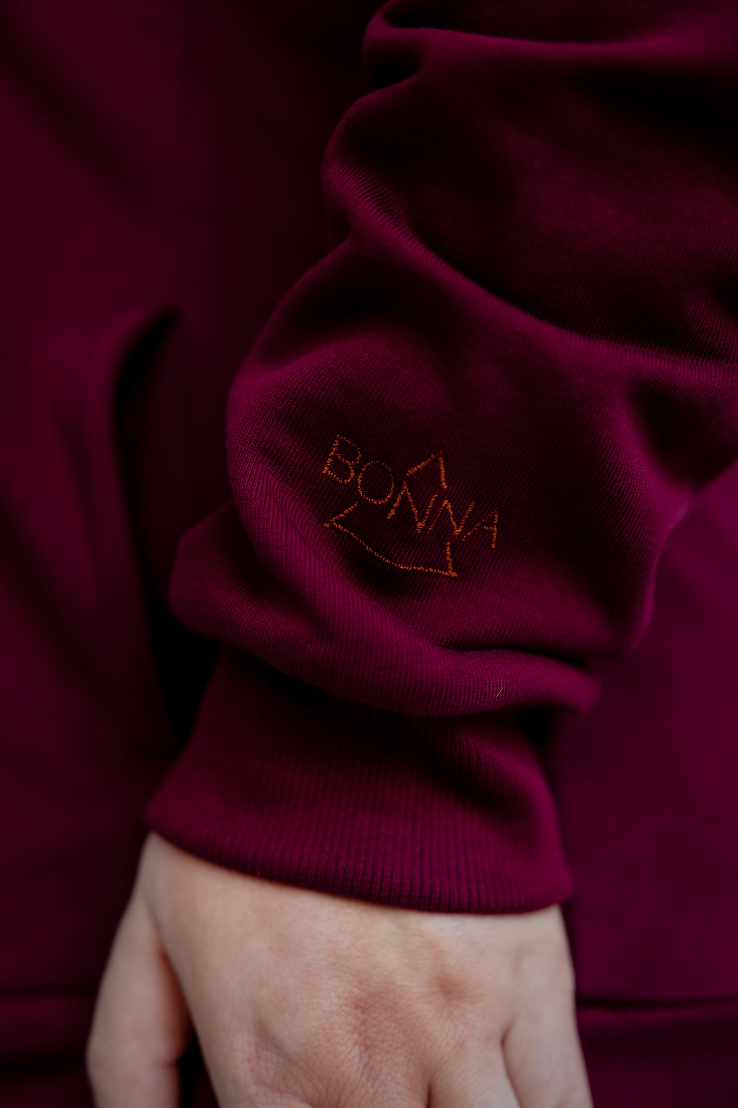 Close-up of a burgundy sweater sleeve with 'BONNA' embroidered on it.