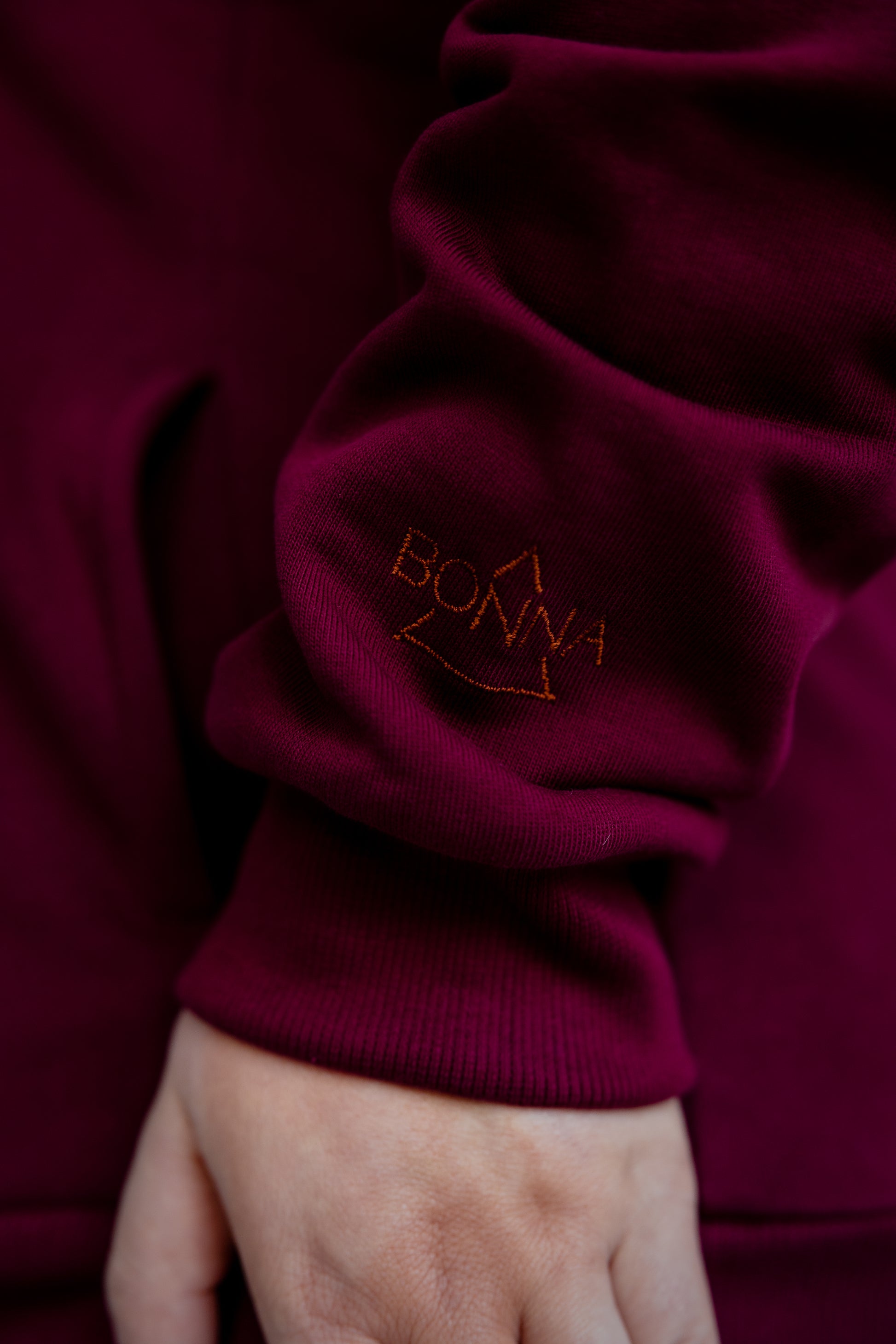 Close-up of a burgundy sweater sleeve with 'BONNA' embroidered on it.