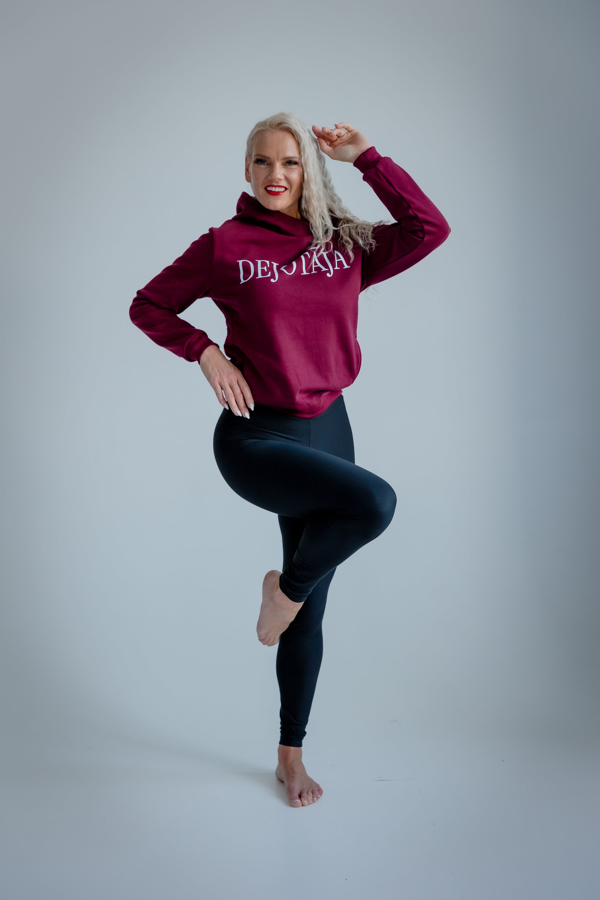 Person wearing a maroon hoodie with text and black leggings on a gray background