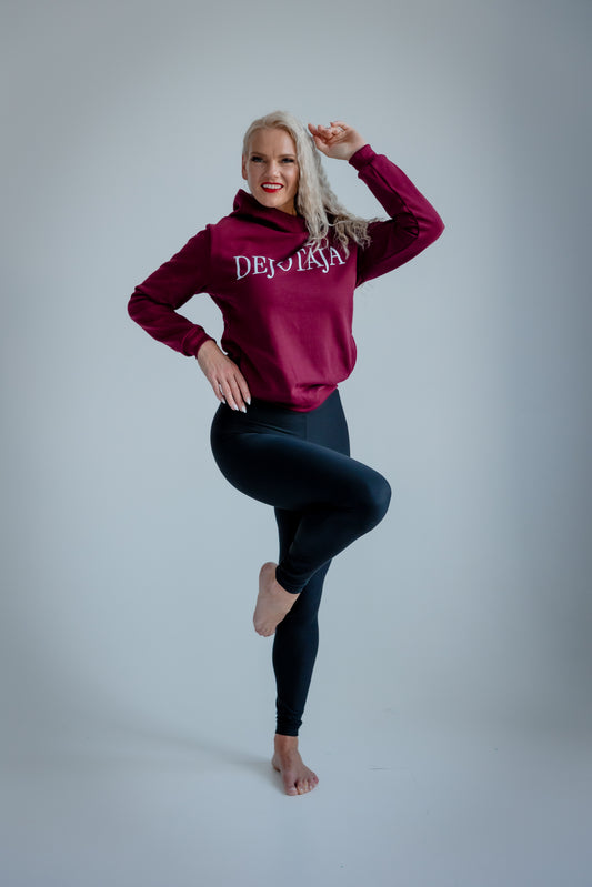 Person wearing a maroon hoodie with text and black leggings on a gray background