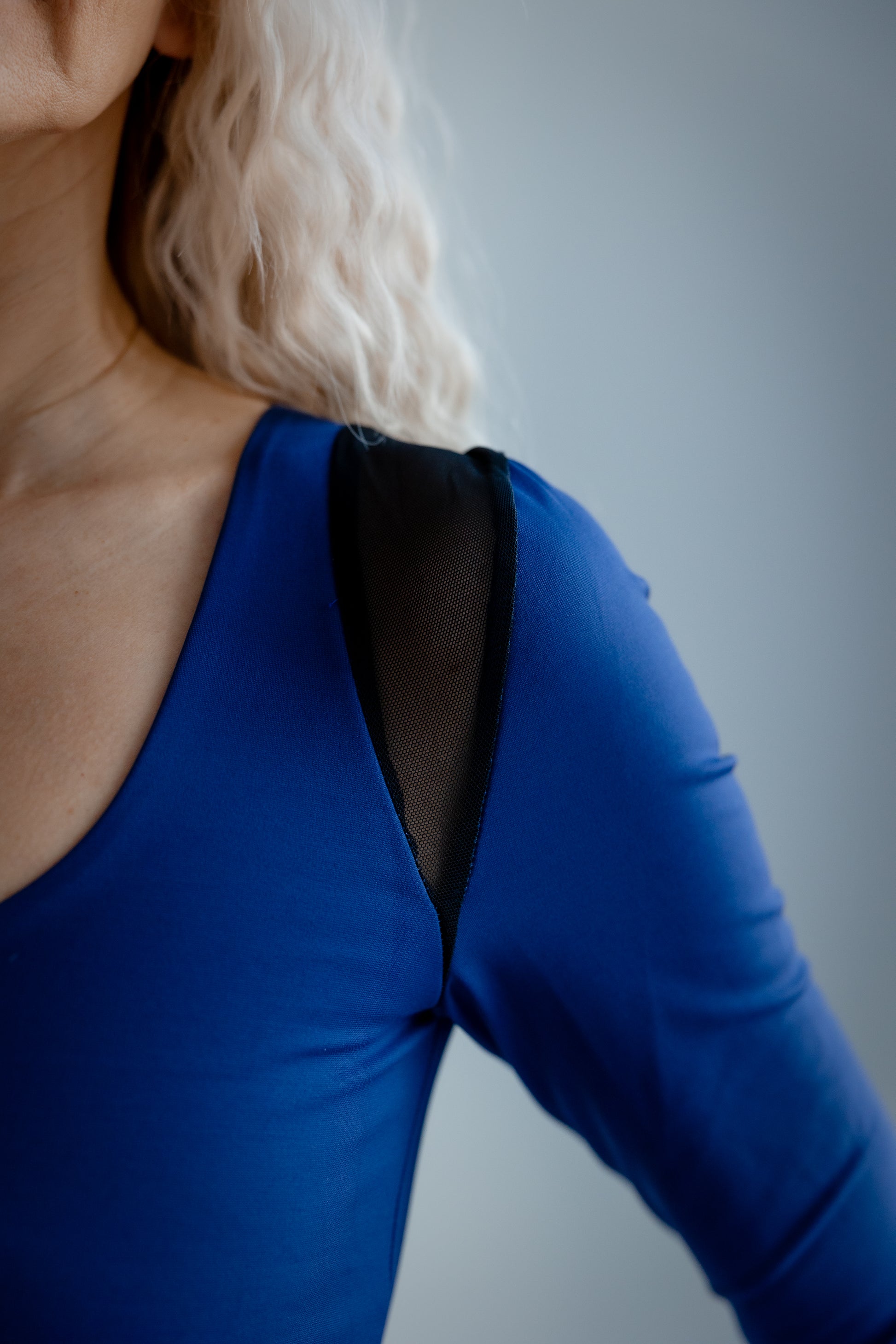 Blue long-sleeve top with a black mesh panel on a plain background