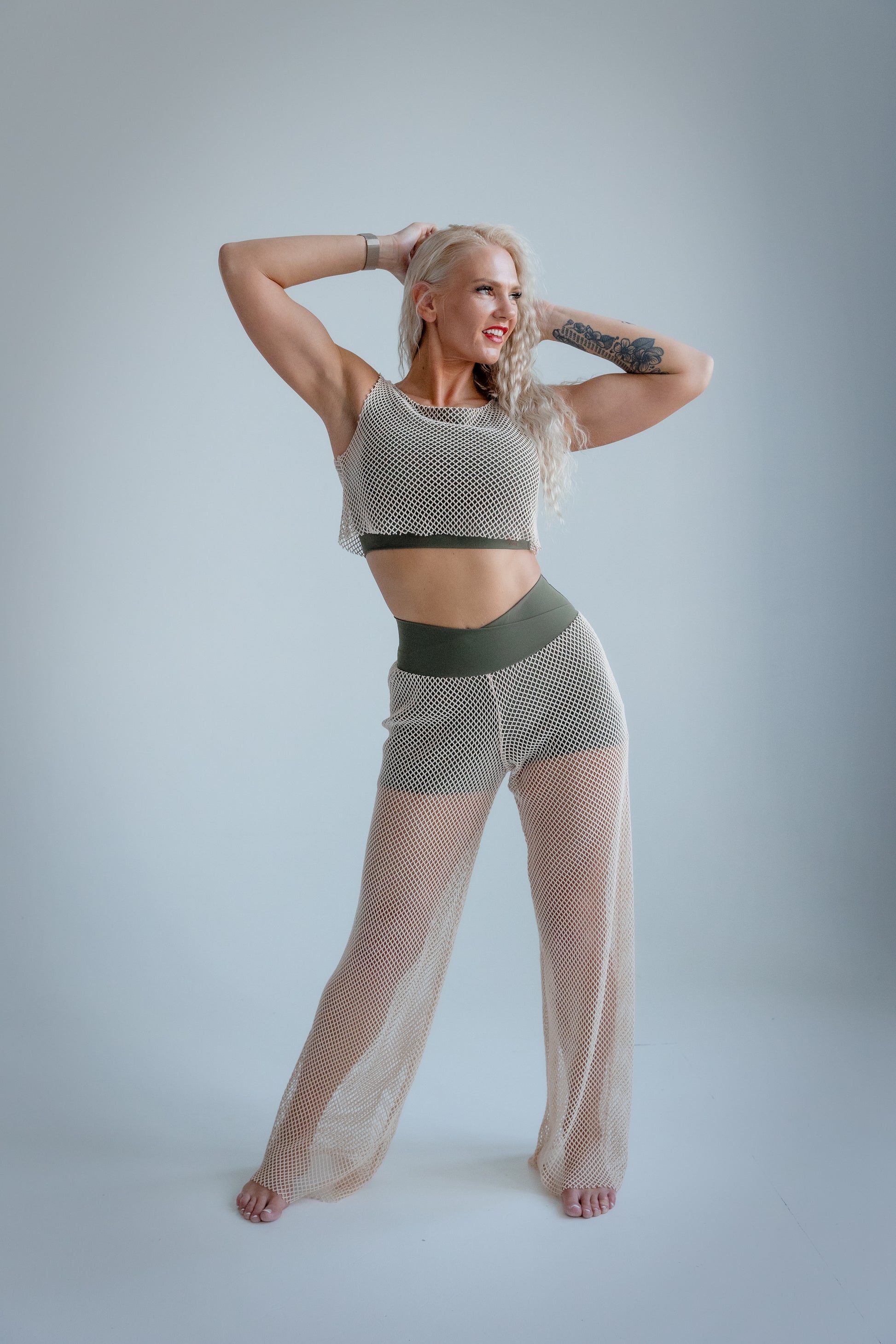 Woman wearing a fishnet top and pants on a plain background