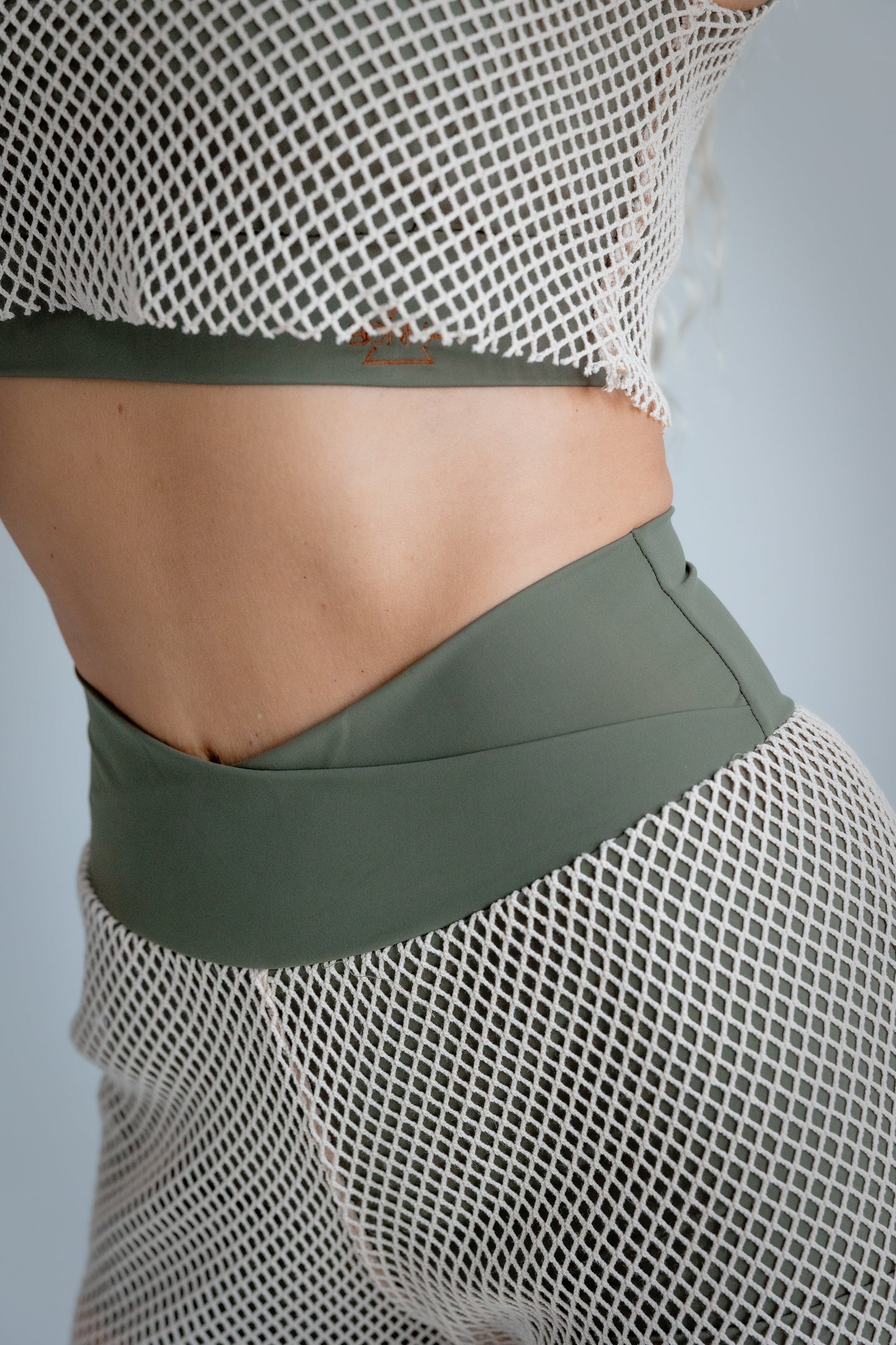 Person wearing a green sports bra and shorts with a mesh top on a gray background
