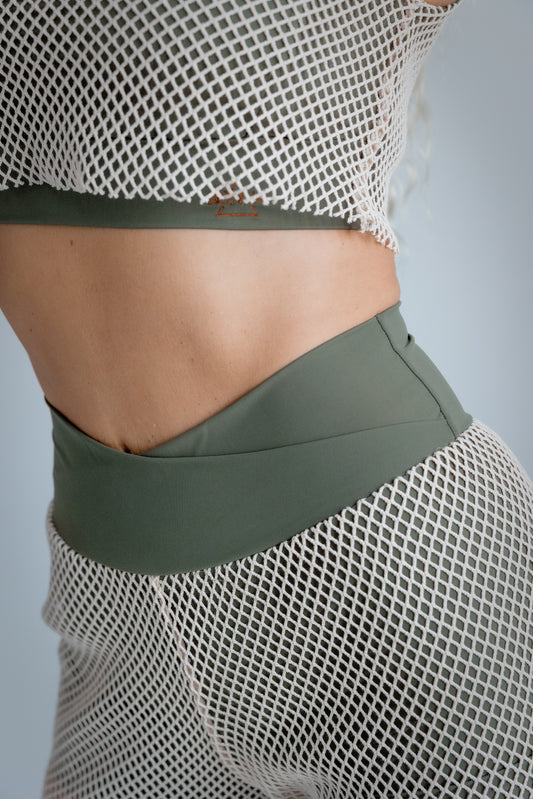 Person wearing a green sports bra and shorts with a mesh top on a gray background