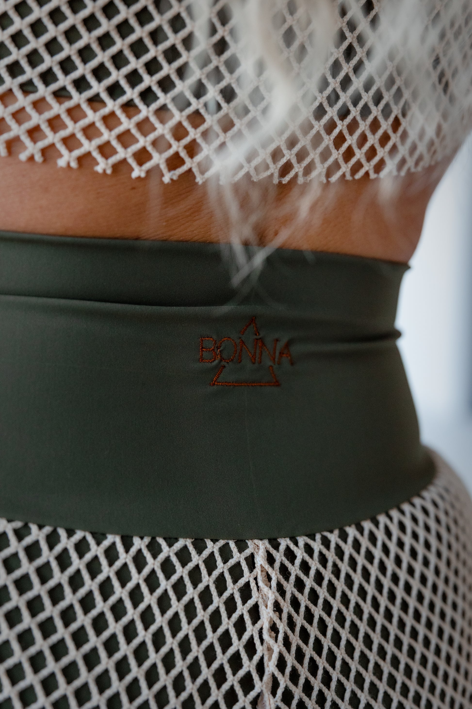 Mannequin wearing a green belt with 'BONNA' logo and fishnet top.