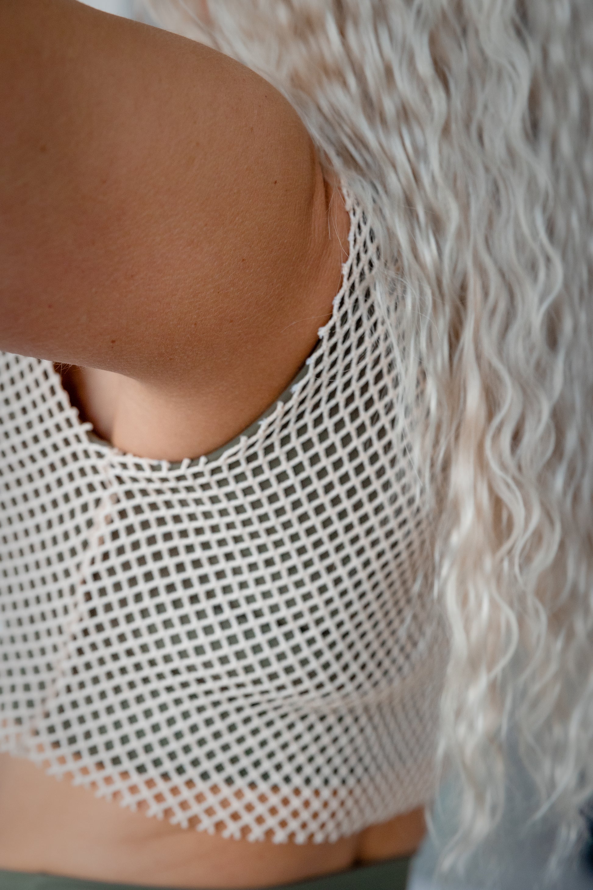 Close-up of a person wearing a white fishnet top with a blurred background