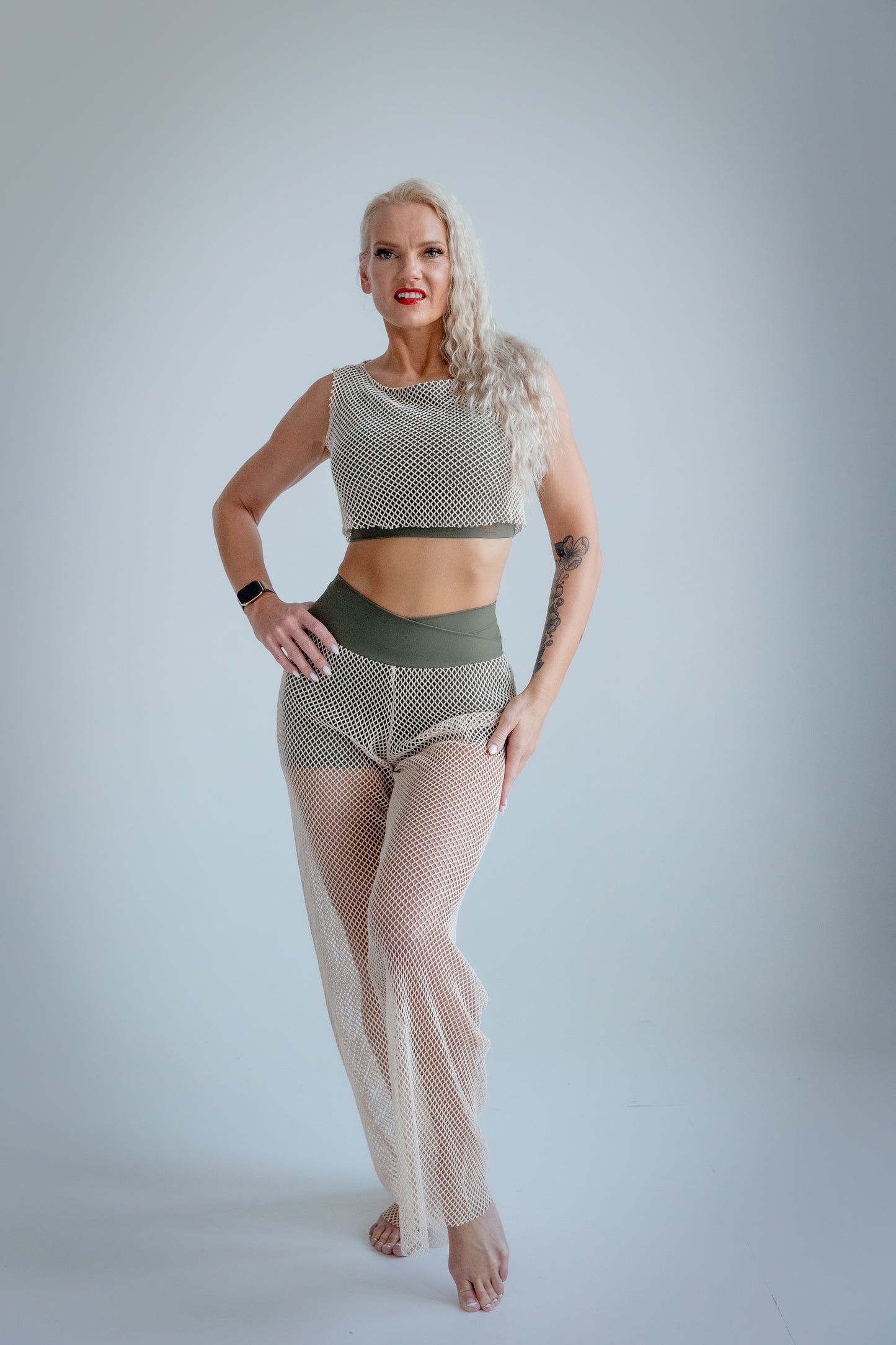 Woman wearing a patterned top and fishnet pants on a plain background