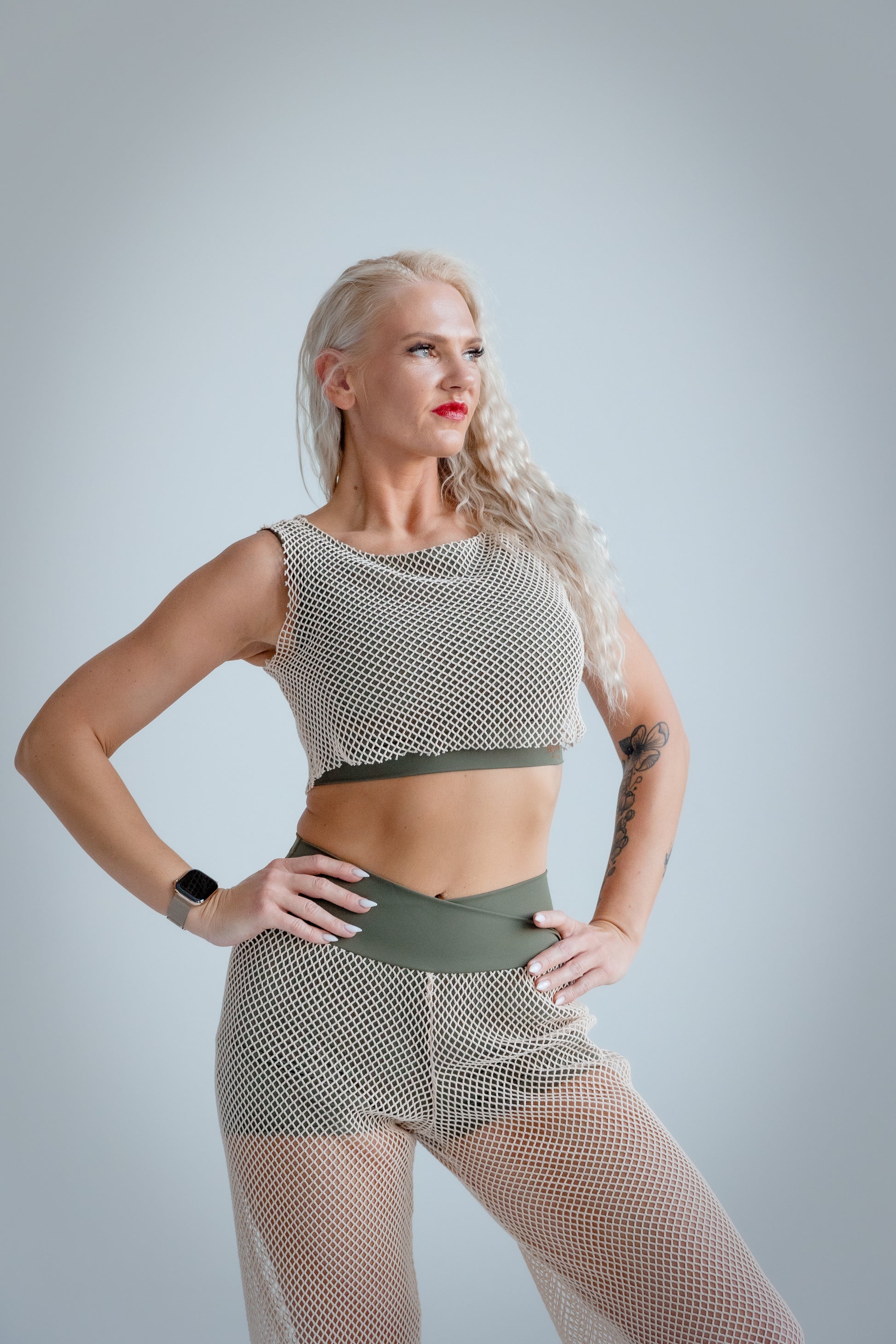 Woman wearing a fishnet top and pants against a plain background