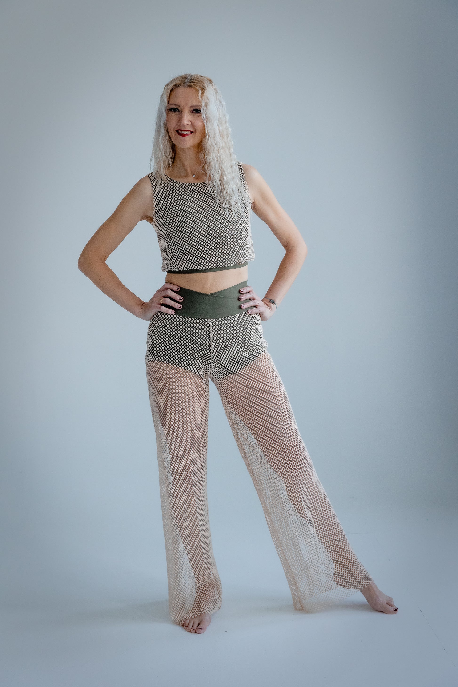 Woman wearing a patterned top and sheer pants on a plain background