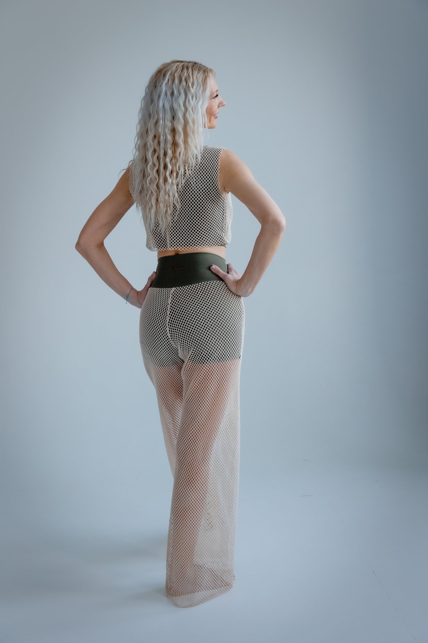 Woman wearing a patterned top and sheer pants against a plain background