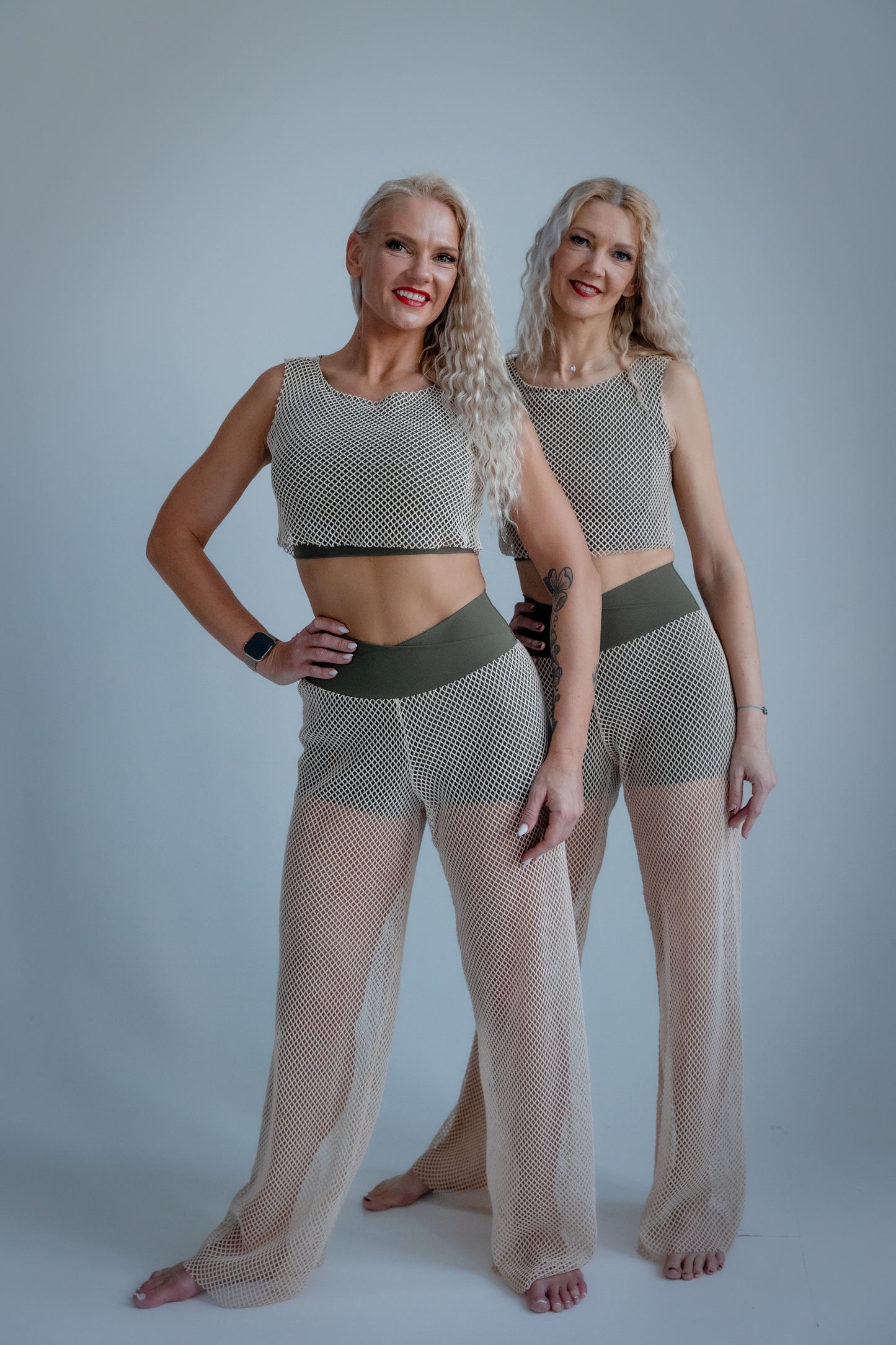 Two women wearing matching fishnet outfits against a plain background