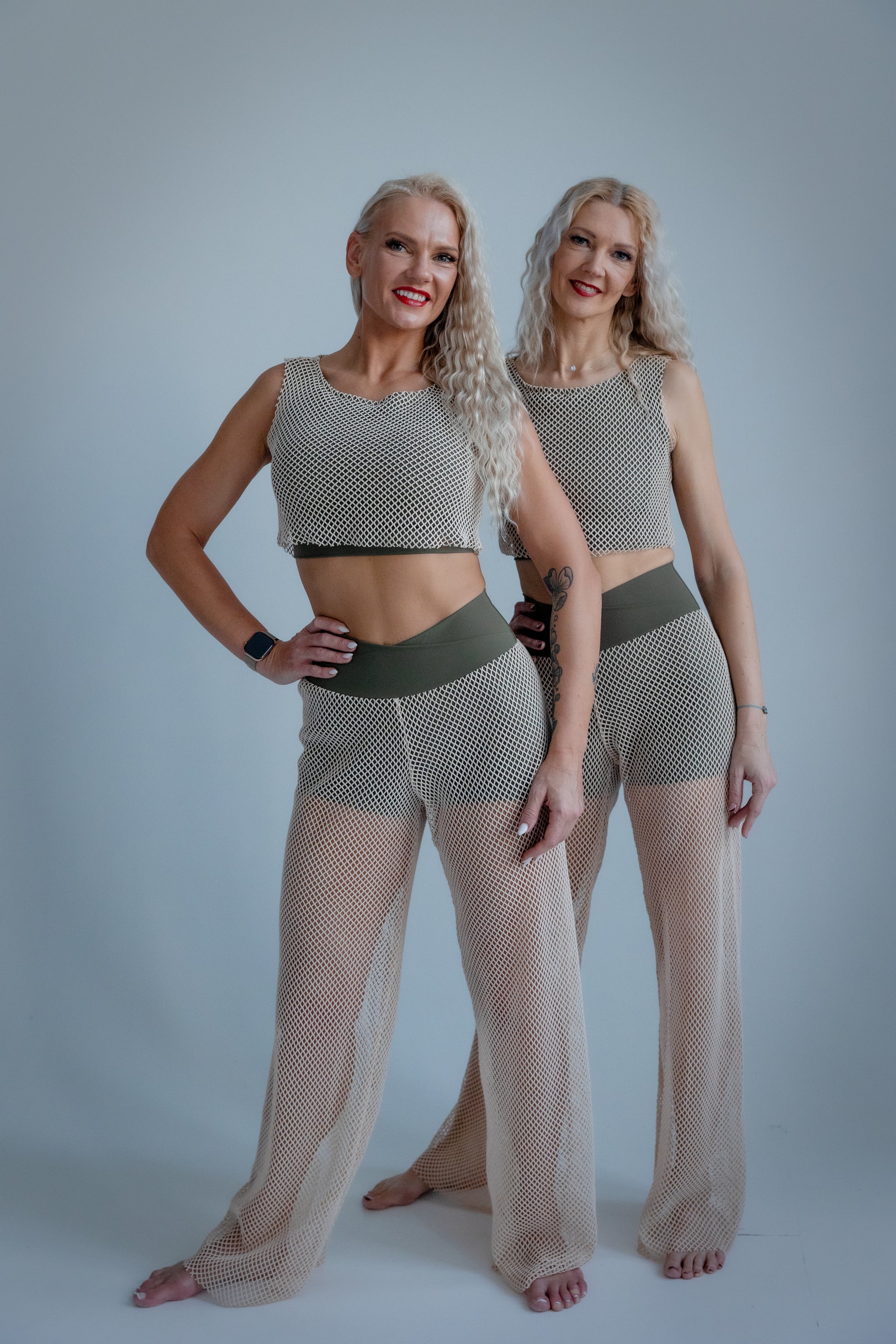 Two women wearing matching fishnet outfits against a plain background